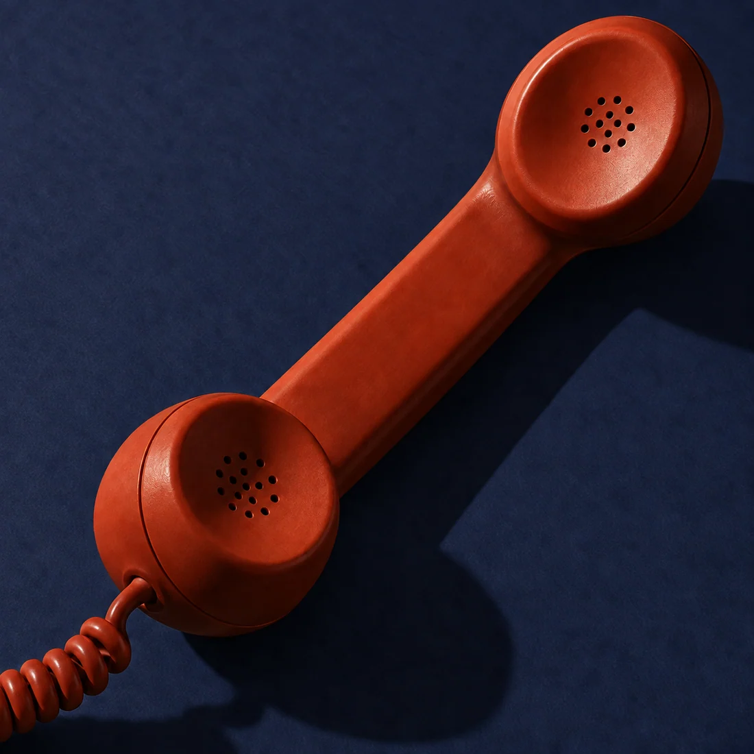 Conceptual editorial image of a rust-red telephone handset on an ink-blue background.